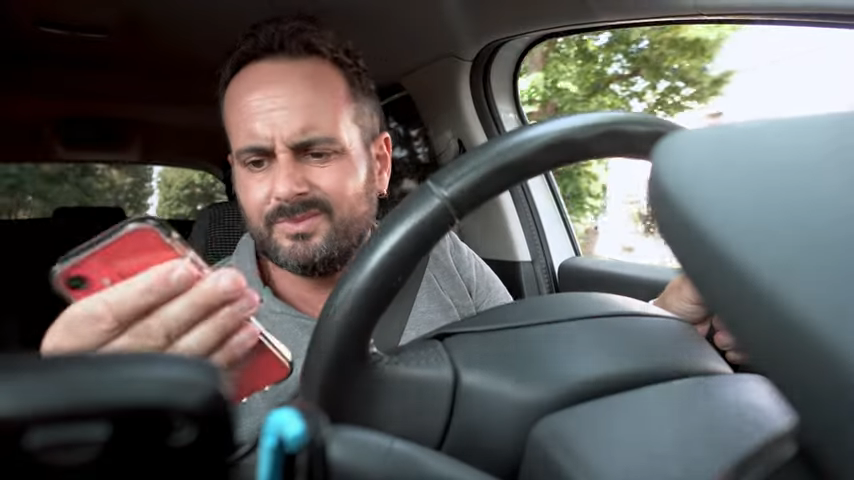 uomo al volante guarda telefono